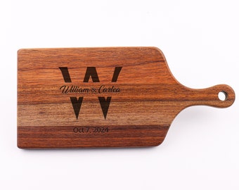 May include: A wooden cutting board with a handle, engraved with the initials "W" and the text "William & Carlea Oct 7, 2024".