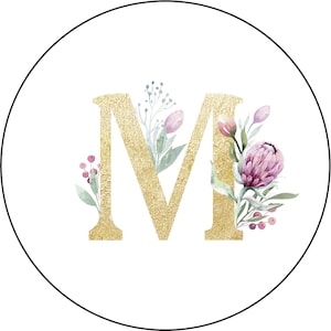 May include: A gold letter M with a floral design. The flowers are pink, white, and green. The letter is on a white background.