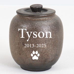 Peut inclure: Urne funéraire pour animaux de compagnie en céramique marron moucheté, avec couvercle et petit bouton. Le nom "Tyson" est imprimé en blanc, avec les années "2013-2025" et une empreinte de patte blanche.