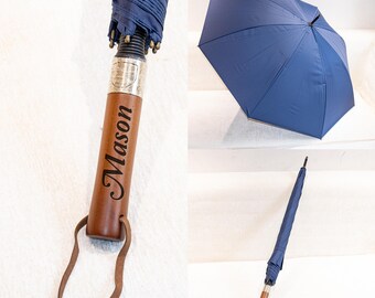 May include: A navy blue umbrella featuring a wooden handle engraved with the name Mason in a script font. The handle includes a silver-toned metal collar and a brown leather wrist strap. The umbrella is shown both closed and fully opened.