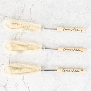 Peut inclure: Trois longues et fines brosses de nettoyage blanches avec des manches en bois. Chaque manche est gravé du texte "Charlotte's Kitchen".