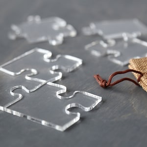 May include: A set of clear acrylic puzzle pieces with a brown drawstring bag. The puzzle pieces are shaped like jigsaw pieces.