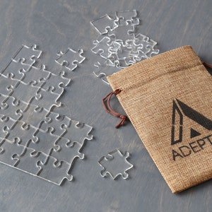 May include: A clear acrylic jigsaw puzzle with a burlap bag featuring the logo "ADEPPTUS" printed in black.