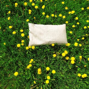 May include: A white linen pillow resting on a bed of green grass with yellow dandelions.