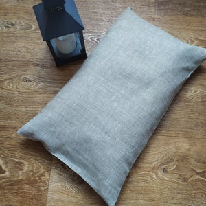 May include: A light gray linen pillow with a subtle texture. The pillow is lying on a wooden floor.