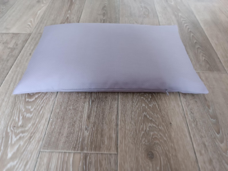 May include: A light purple rectangular pillow on a wood floor.