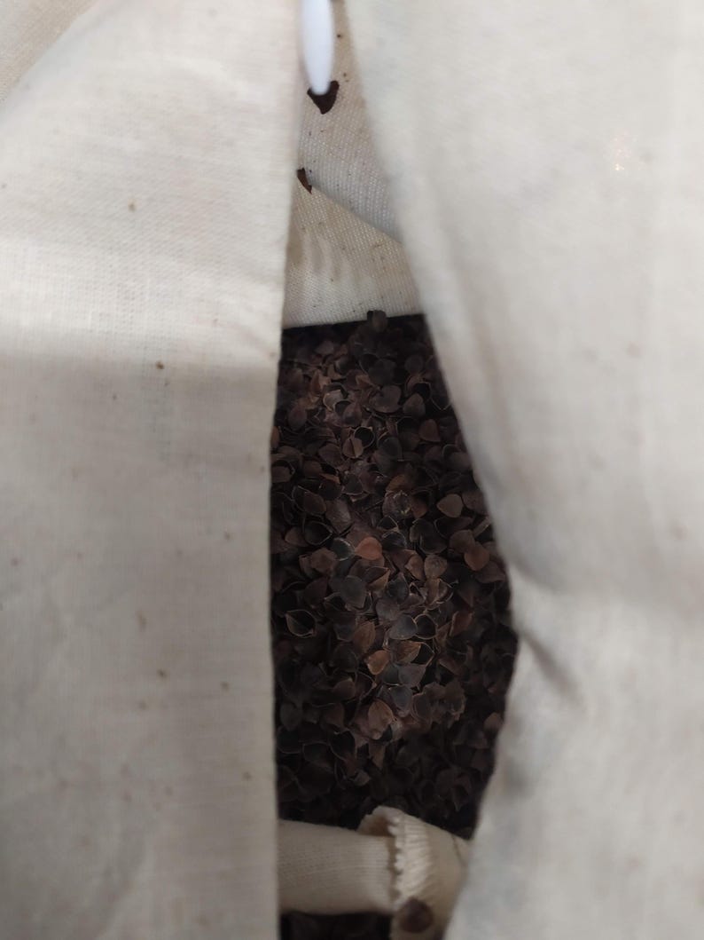 May include: A white fabric bag filled with buckwheat hulls. The bag is open at the top, revealing the brown hulls inside.