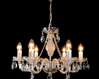 May include: A crystal chandelier with six lights and a silver chain hanging from the ceiling. The chandelier has a clear glass design with many crystal drops.