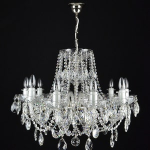 May include: A silver chandelier with crystal drops and clear glass candle holders. The chandelier has a traditional design and is perfect for a formal dining room or living room.