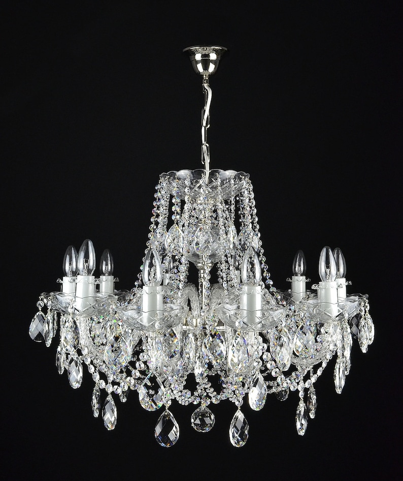 May include: A silver chandelier with crystal drops and clear glass candle holders. The chandelier has a traditional design and is perfect for a formal dining room or living room.