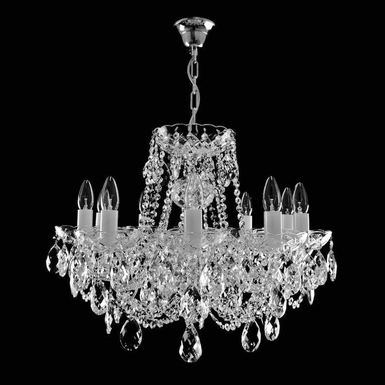 May include: A crystal chandelier with a silver finish and clear glass crystals. The chandelier has eight light bulbs and is hanging from a chain.
