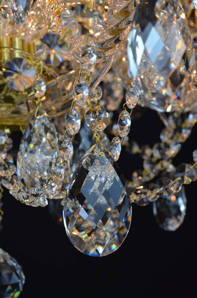May include: Close-up of a crystal chandelier with a large, faceted crystal pendant hanging from a gold chain. The crystal is reflecting light, creating a rainbow effect.