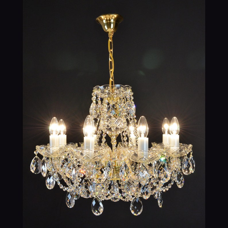 May include: A gold chandelier with crystal accents and multiple light bulbs. The chandelier has a traditional design with a central, round, crystal-covered fixture and cascading crystal strands.