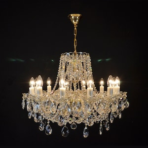 May include: A crystal chandelier with a gold finish and multiple arms, each with a clear glass bulb. The chandelier is adorned with numerous crystal drops, creating a sparkling effect.