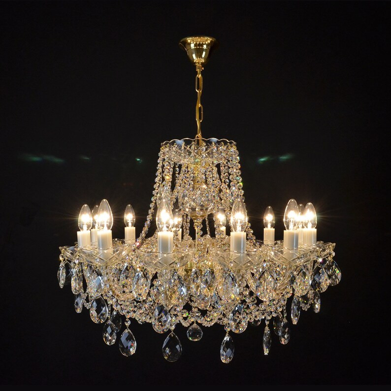 May include: A crystal chandelier with a gold finish and multiple arms, each with a clear glass bulb. The chandelier is adorned with numerous crystal drops, creating a sparkling effect.