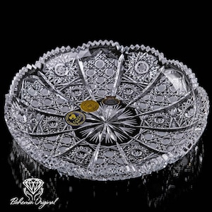 May include: A clear, cut crystal bowl with detailed geometric patterns. The bowl features a starburst design in the centre and a scalloped edge. The bowl has a Bohemia Original logo and several stickers.