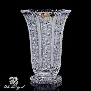 以下が含まれることがあります： 広口でフレアトップ、詳細な模様のデザインが施された透明なクリスタル花瓶。 縦のパネルと複雑なスターバーストと円形のパターンが特徴です。 ベースは丸く、模様も入っています。 花瓶にはBohemia Originalのロゴが入っています。