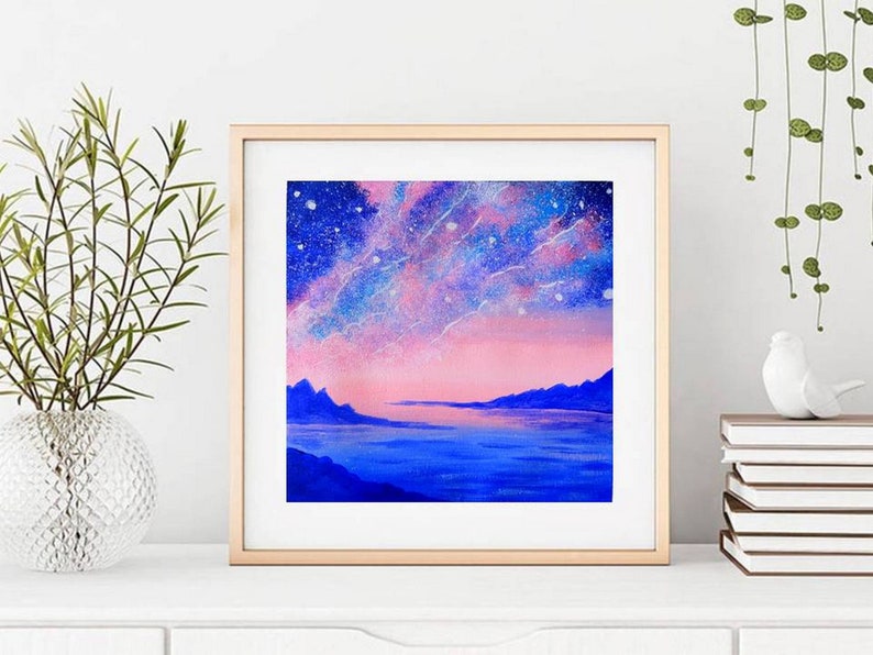 May include: A framed painting of a pink and blue landscape with a starry sky and mountains in the distance. The painting is in a light wood frame.