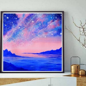May include: A framed painting of a pink and blue starry sky over a dark blue body of water with mountains in the distance.