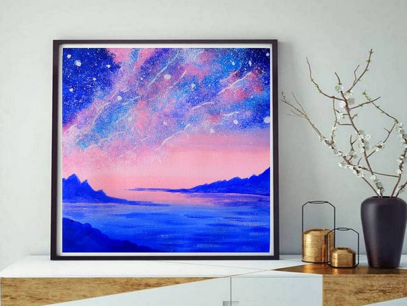 May include: A framed painting of a pink and blue starry sky over a dark blue body of water with mountains in the distance.