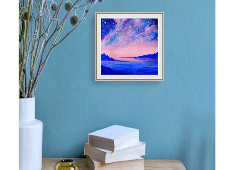 May include: A framed painting of a pink and blue landscape with a starry sky and a body of water in the foreground.