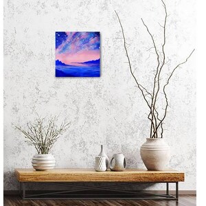 May include: A painting of a pink and blue sky with stars over a dark blue body of water. The water reflects the pink and blue colors of the sky. There are mountains in the distance.