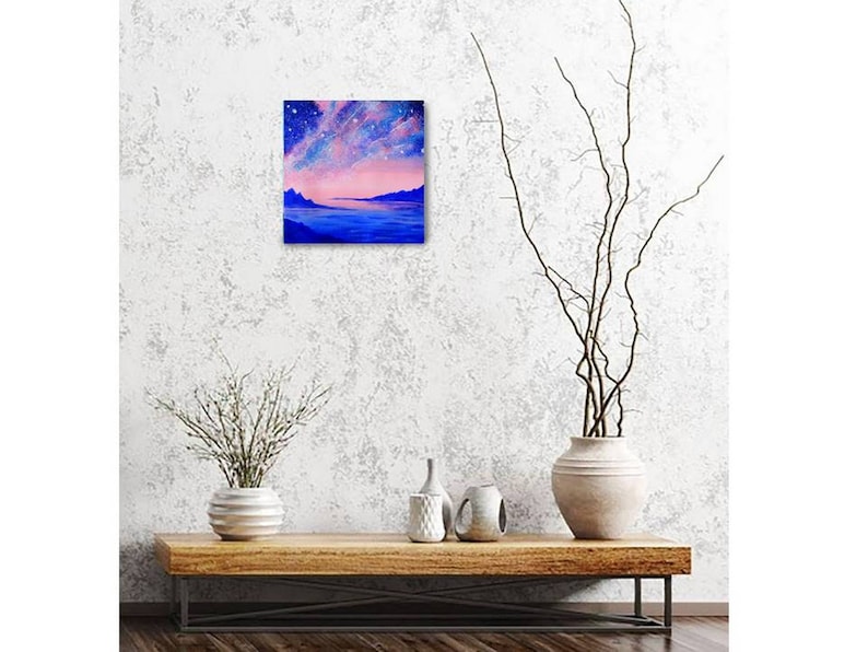 May include: A painting of a pink and blue sky with stars over a dark blue body of water. The water reflects the pink and blue colors of the sky. There are mountains in the distance.
