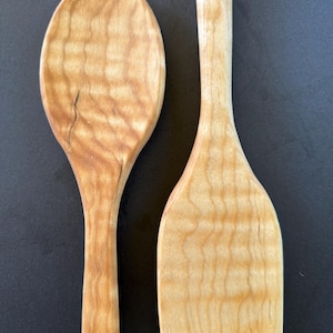 Può includere: Due utensili da cucina in legno, un cucchiaio e una spatola, con un motivo a venature del legno naturale.