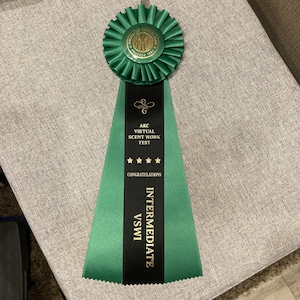 May include: Green and black ribbon with gold lettering. The ribbon reads "AKC Virtual Scent Work Test Congratulations Intermediate VSWI".