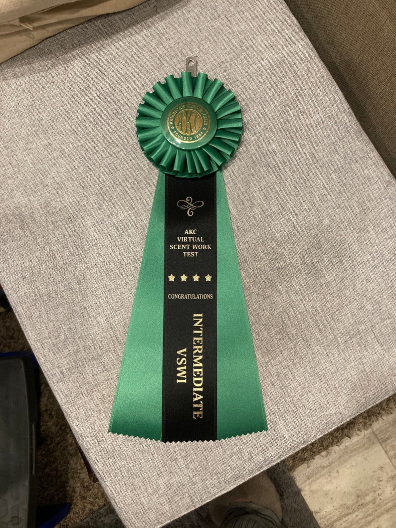 May include: Green and black ribbon with gold lettering. The ribbon reads "AKC Virtual Scent Work Test Congratulations Intermediate VSWI".
