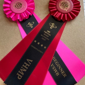 May include: Two red and pink ribbons with black stripes and gold lettering. The ribbons say "AKC Virtual Home Manners Test Congratulations" and "Beginner VSWB".