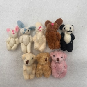 May include: A collection of small, handmade stuffed animal toys. The assortment includes teddy bears, bunnies, and a panda bear, in various colors such as white, brown, and pink. Each toy has embroidered facial features.