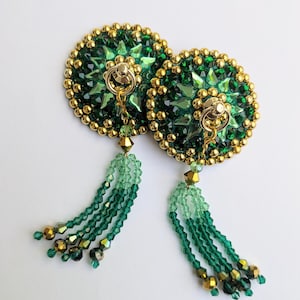 May include: Pair of green and gold beaded nipple pasties. Each pastie features a circular design with green and gold beads, a gold ring, and a beaded tassel. The tassels have a gradient of green and gold beads.
