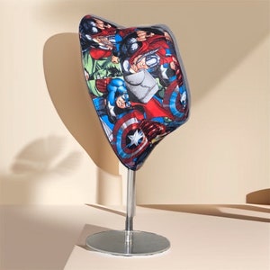May include: A blue and red bucket hat with a graphic print of various superheroes, including Captain America and Thor. The hat is displayed on a silver stand.