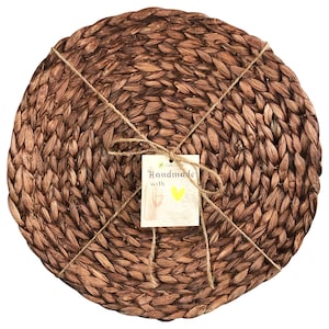 May include: Set of four brown woven round placemats. The placemats are made of natural materials and have a rustic look. The placemats are tied together with twine and a tag that says "Handmade with Love".