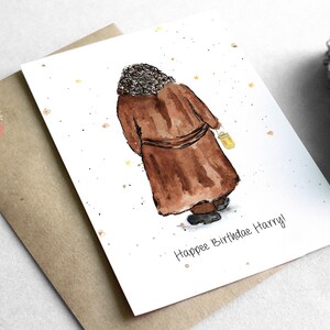 May include: A watercolor illustration of a person in a brown robe holding a yellow lantern. The background is white with gold glitter. The text "Happy Birthday Harry!" is written at the bottom of the card.