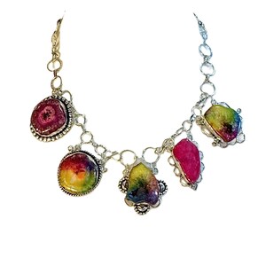 Könnte beinhalten: Eine silberfarbene Halskette mit fünf bunten, unregelmäßig geformten Anhängern. Die Anhänger sind eine Mischung aus Rosa, Gelb und Lila mit einem silbernen Rand. Die Halskette hat ein Kettenglied-Design.