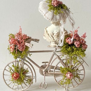 May include: A white vintage-style bicycle with pink flowers in the baskets and a white fabric hat with pink flowers on top of the seat.