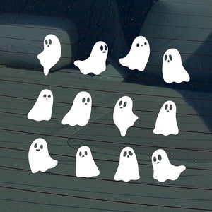 May include: A car window with a collection of white ghost stickers. The ghosts are arranged in rows and have simple black eyes.