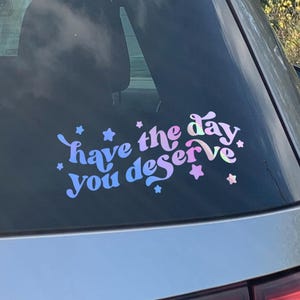 May include: A silver car with a sticker on the back window that says "Have the day you deserve" in a purple and blue gradient font with stars around the text.