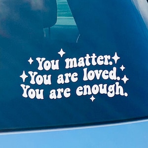 May include: A white vinyl sticker with the text "You matter. You are loved. You are enough." on a blue car window.