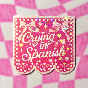Pink holographic sticker with scalloped papel picado design and the phrase Crying in Spanish.