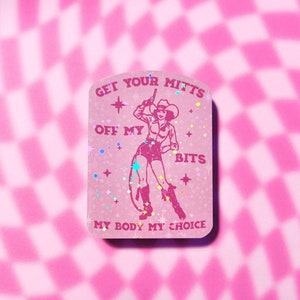 May include: Pink sticker with a glittery background featuring a cowgirl with a gun and the text "Get Your Mitts Off My Bits My Body My Choice".