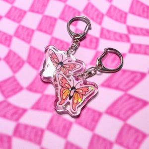 May include: Two pink and orange butterfly keychains with glitter accents. The keychains are made of clear resin and have silver key rings.
