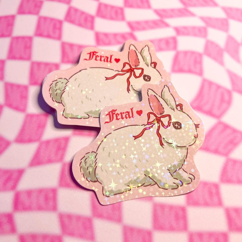 Peut inclure: Deux autocollants repr&eacute;sentant un lapin blanc avec un n&oelig;ud rouge et le mot "Feral". Les autocollants ont une bordure rose et une finition scintillante, sur un fond &agrave; carreaux roses et blancs.