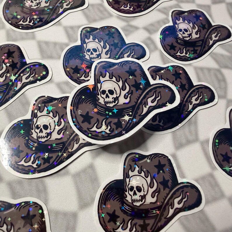 Multiple holographic skull cowboy hat stickers laid out on a greyscale checkered background.