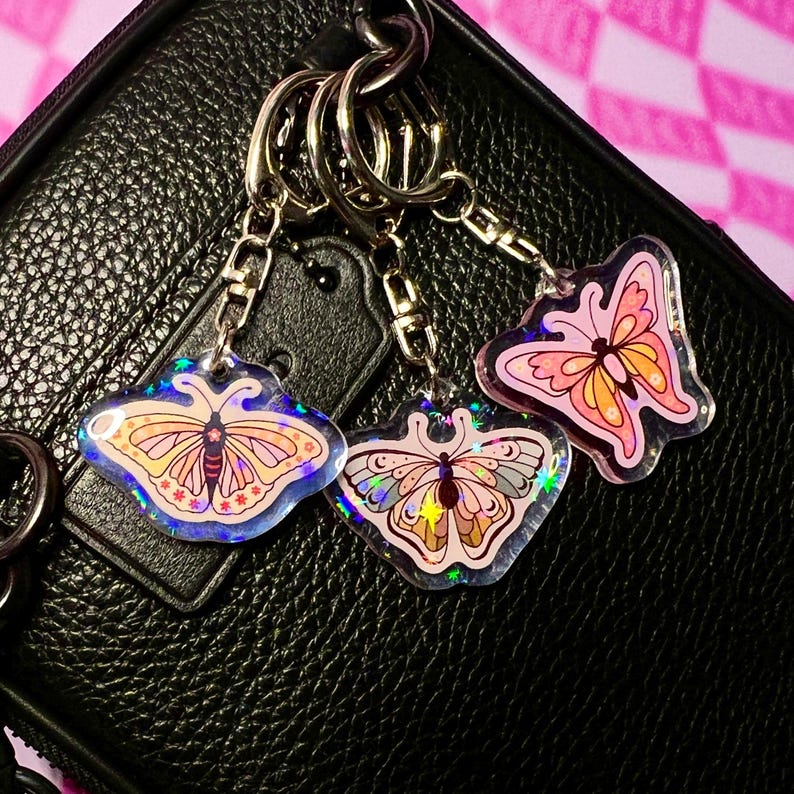 May include: Three iridescent butterfly keychains with gold chain links. The butterflies are pink, orange, and purple with glitter accents.