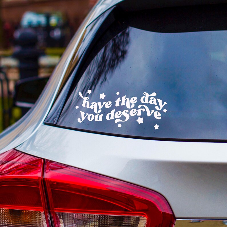 May include: White vinyl sticker on a silver car with the text "have the day you deserve" with white stars around the text.
