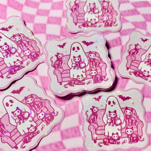 Halloween holographic spooky skeleton cat ghostie sticker with sparkly star laminate on glossy vinyl arranged randomly to show holographic effect.