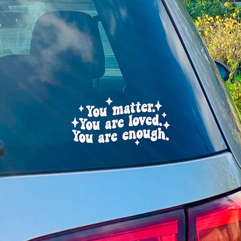 May include: A white vinyl sticker with the text "You matter. You are loved. You are enough." on a blue car window.